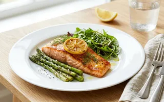 Salmón al horno con espárragos y limón servido en un plato blanco